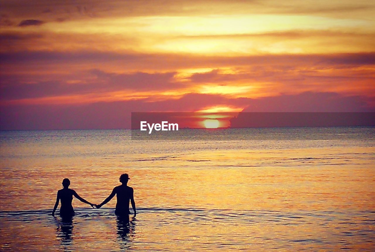 SILHOUETTE OF FRIENDS ON BEACH AGAINST SKY DURING SUNSET