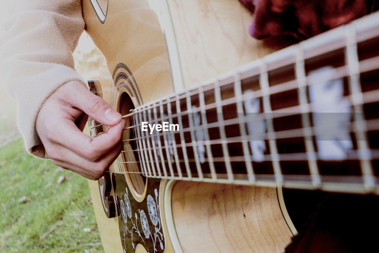 Midsection of person playing guitar on field