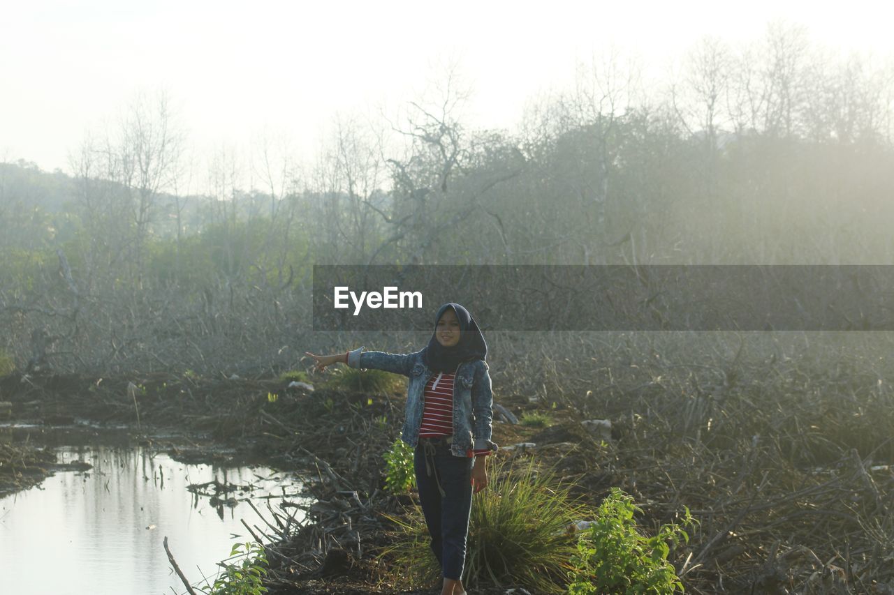 Woman gesturing while standing against bare trees