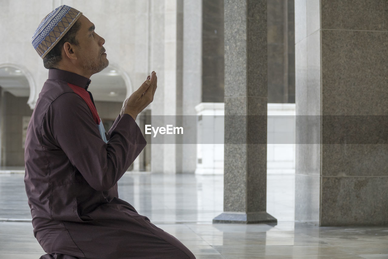 Side view of mature man praying while kneeling at mosque