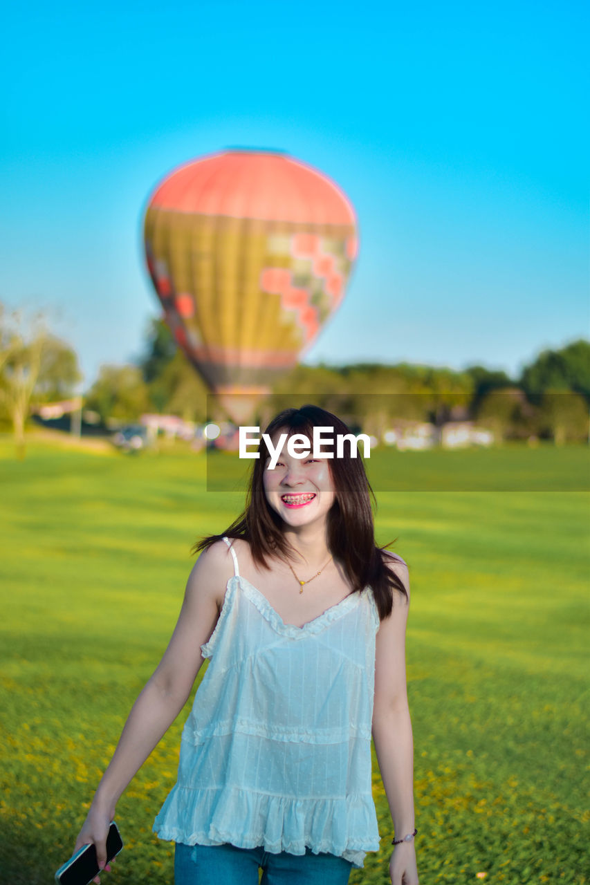 Portrait of young woman with balloons against sky