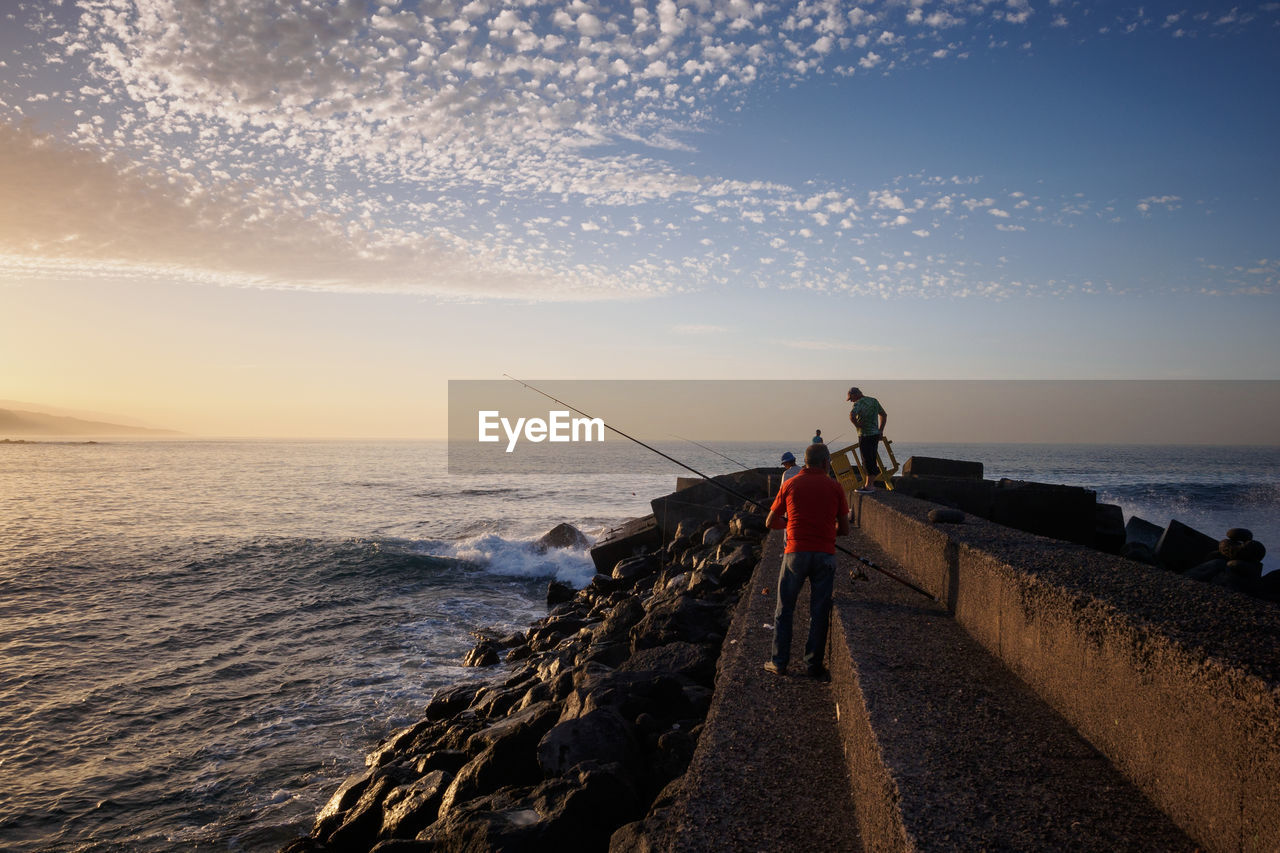 Rear view of men on wall fishing in sea