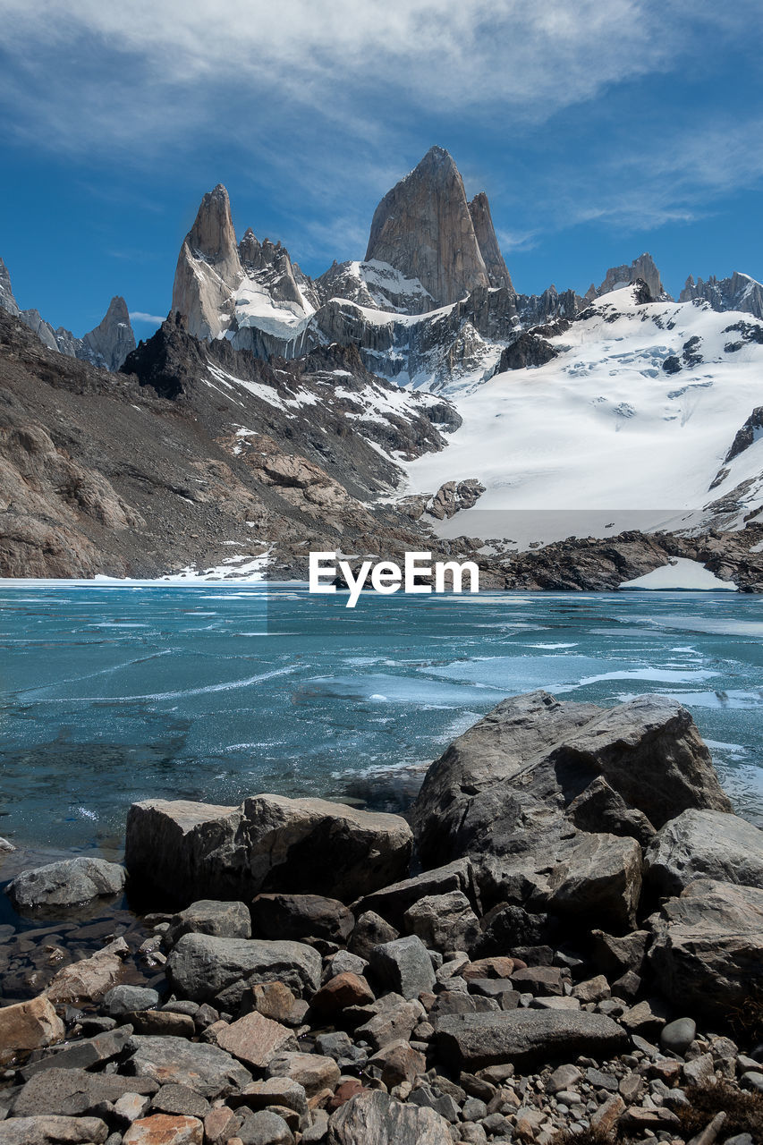 Scenic view of sea by snowcapped mountains against sky