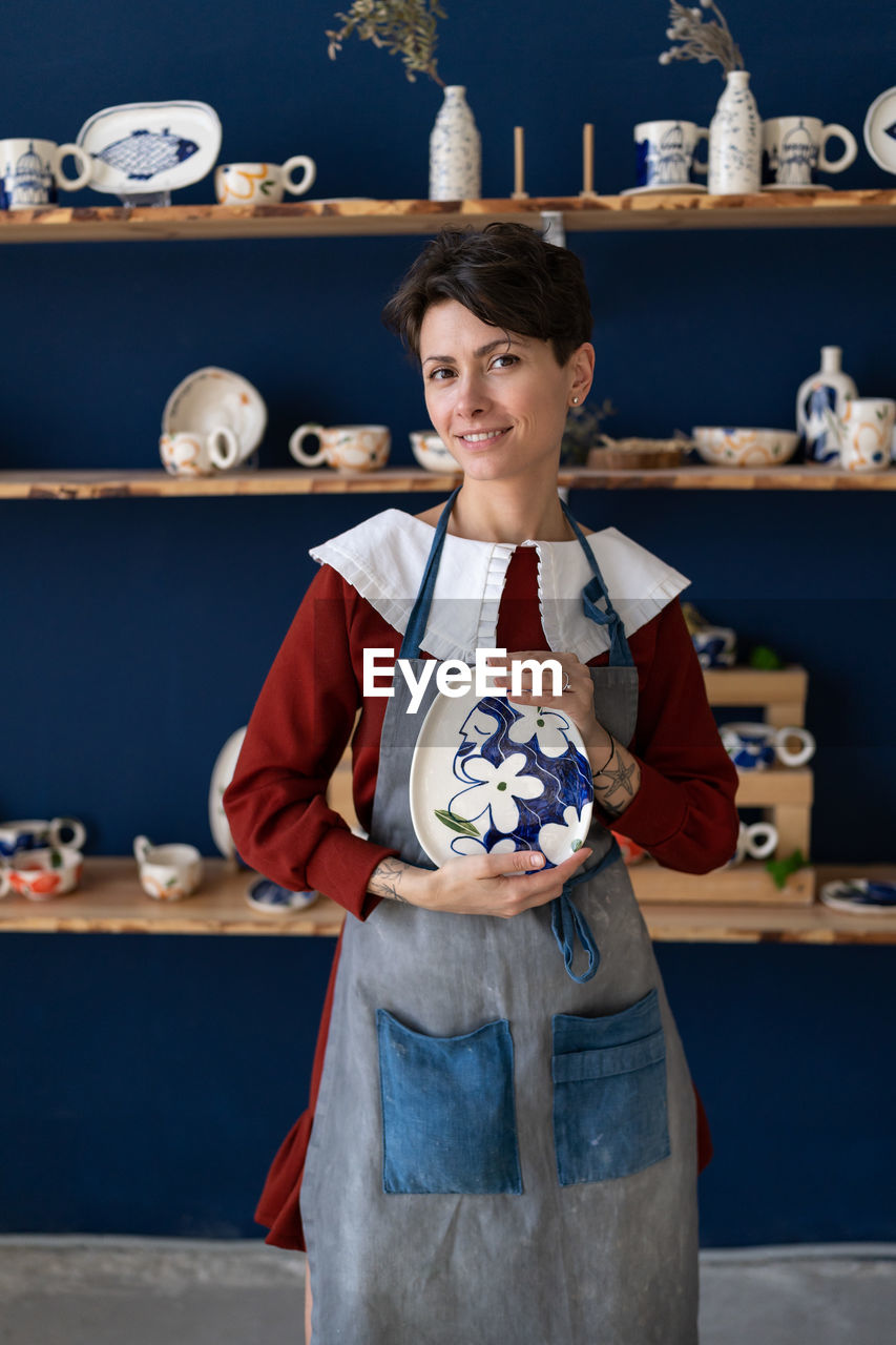 Successful ceramics studio owner posing with handmade plate at workplace