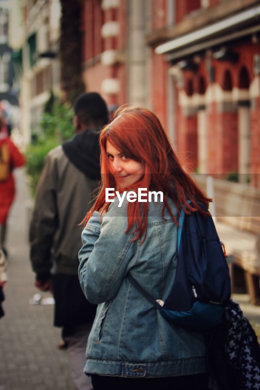 Redhead woman smiling while standing on sidewalk in city