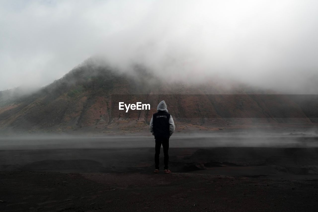 FULL LENGTH REAR VIEW OF MAN STANDING ON LANDSCAPE IN FOGGY WEATHER