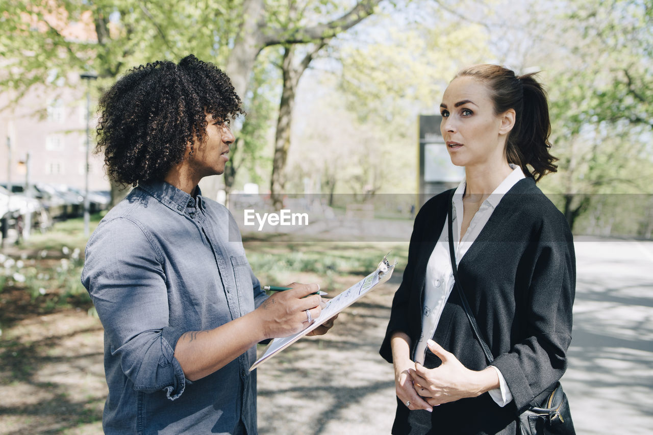 Confident businessman discussing with female colleague while standing on road