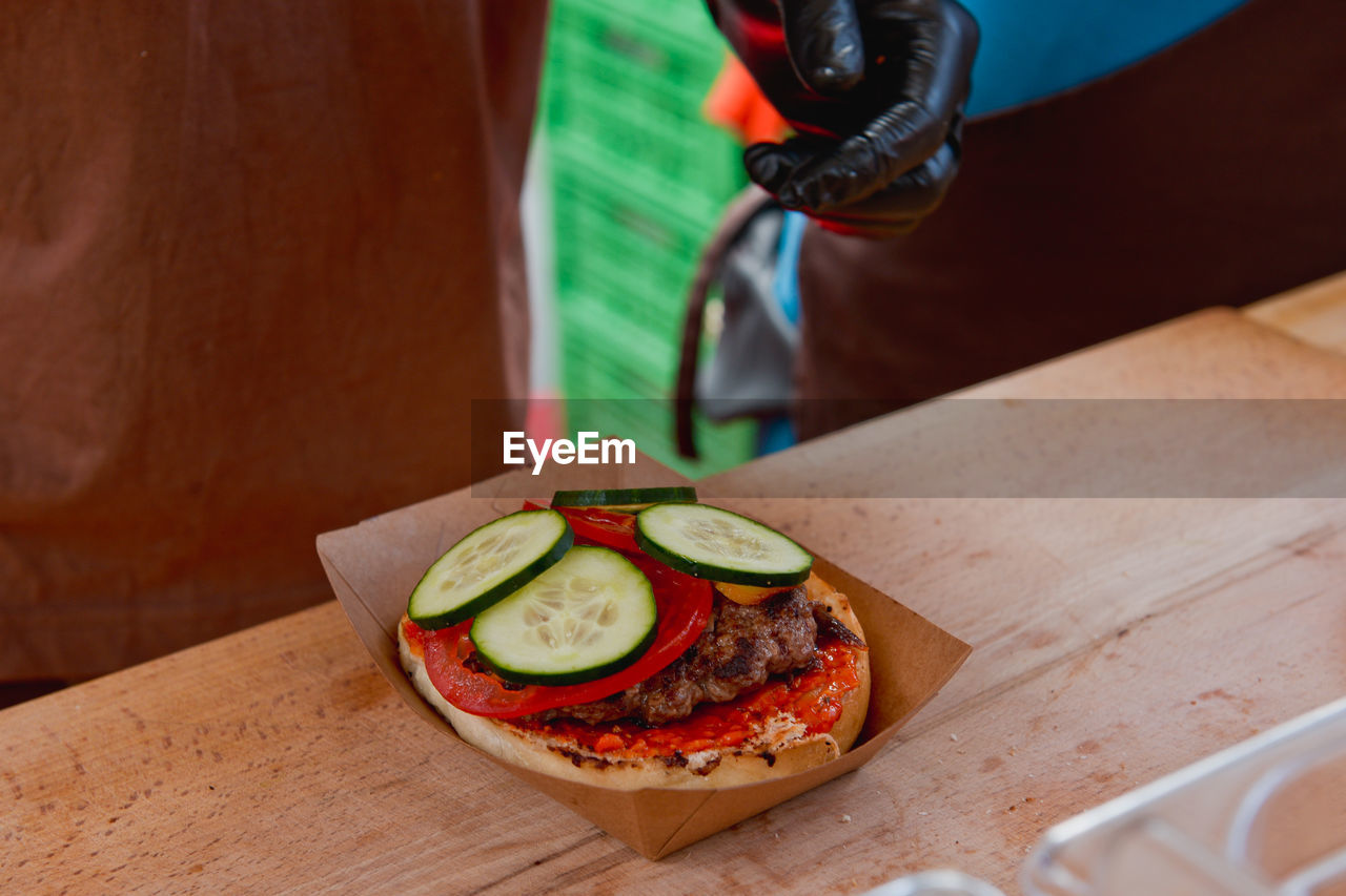 Cropped image of vendor preparing hamburger on table at market