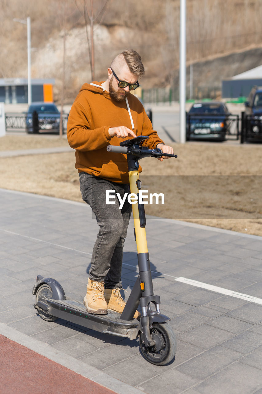 side view of man riding push scooter on road