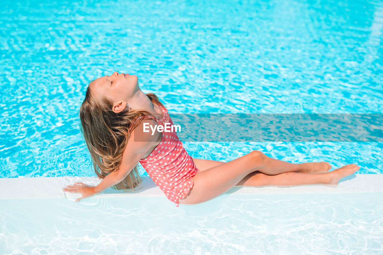 Side view of girl sitting by swimming pool