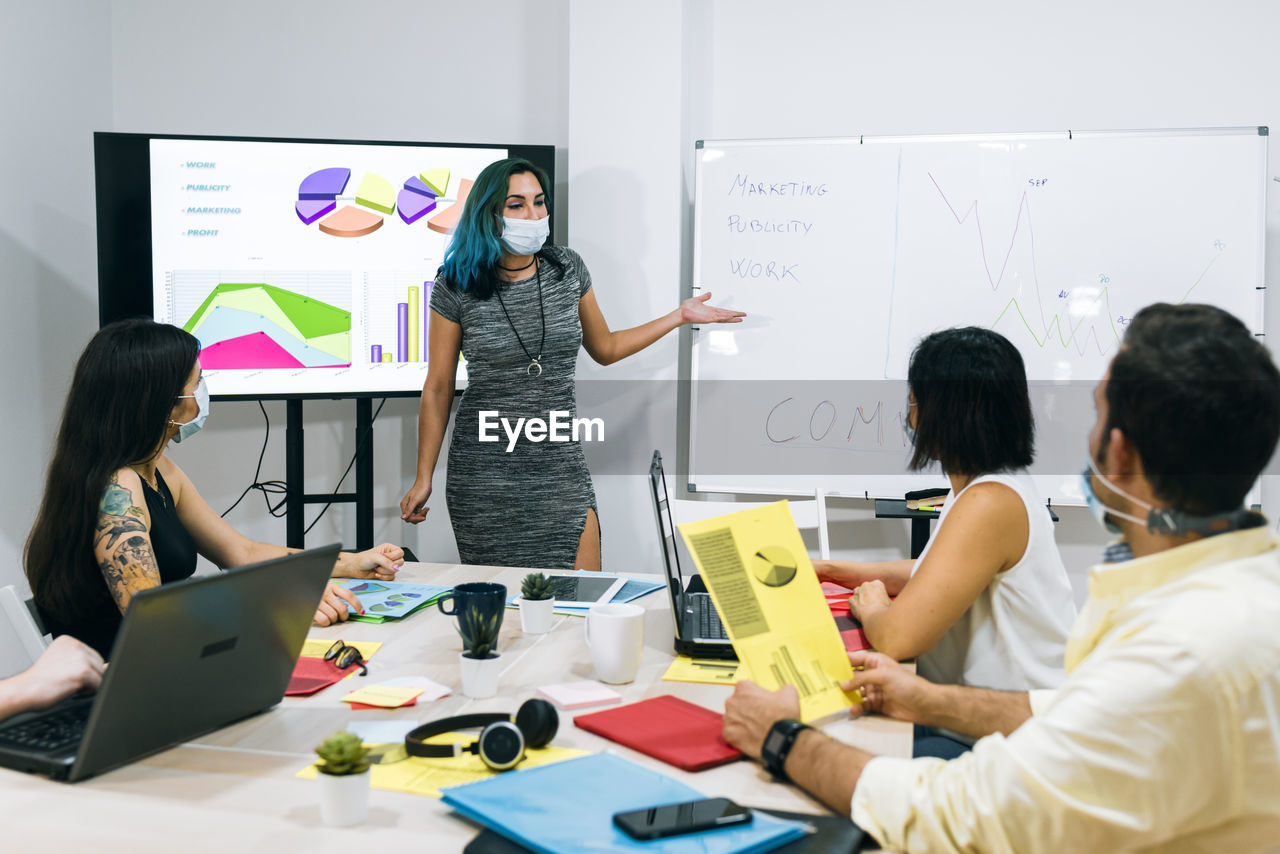 A young woman with a mask leading a work group in the office