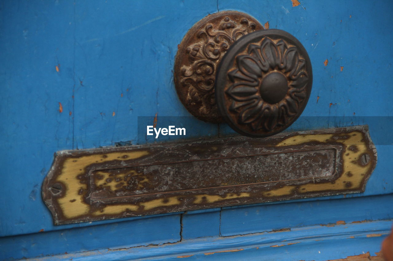 Close-up of rusty handle and mailbox mounted on wooden door