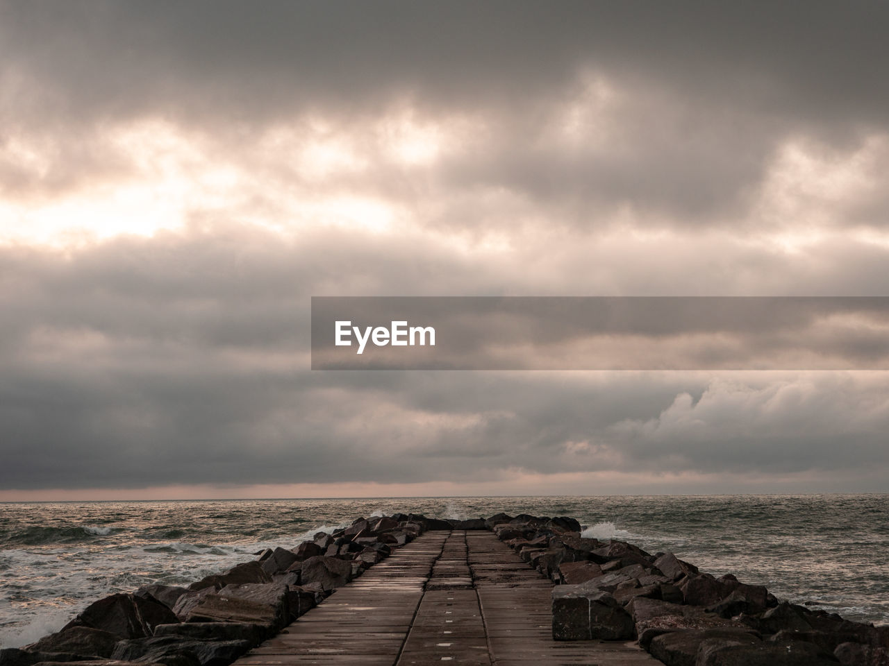 PIER OVER SEA AGAINST CLOUDY SKY