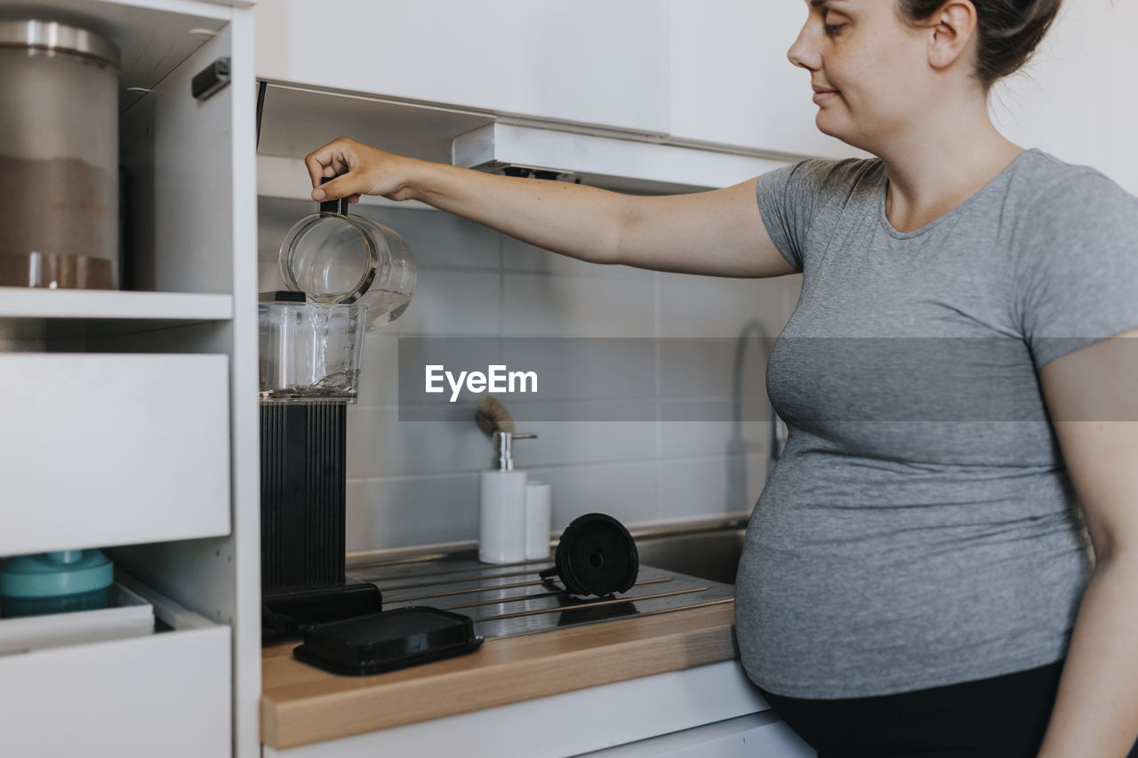 Pregnant woman preparing coffee in kitchen