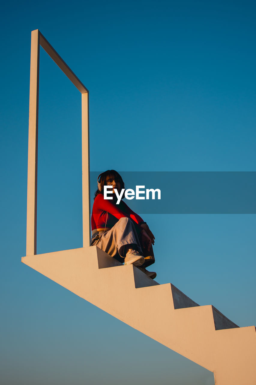 LOW ANGLE VIEW OF WOMAN STANDING AGAINST CLEAR SKY