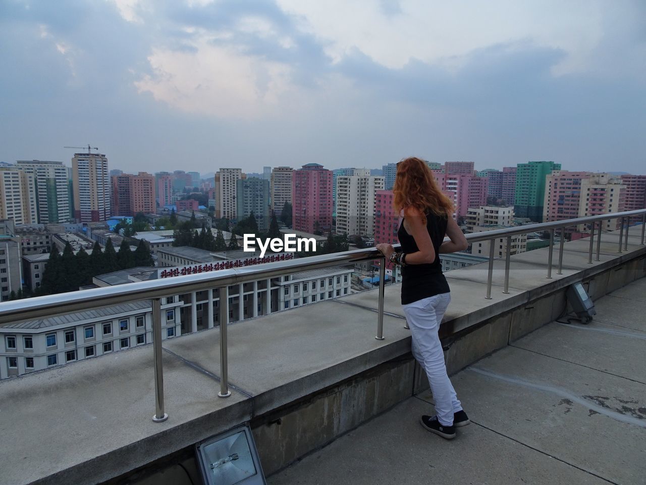 Full length of woman looking at cityscape against cloudy sky