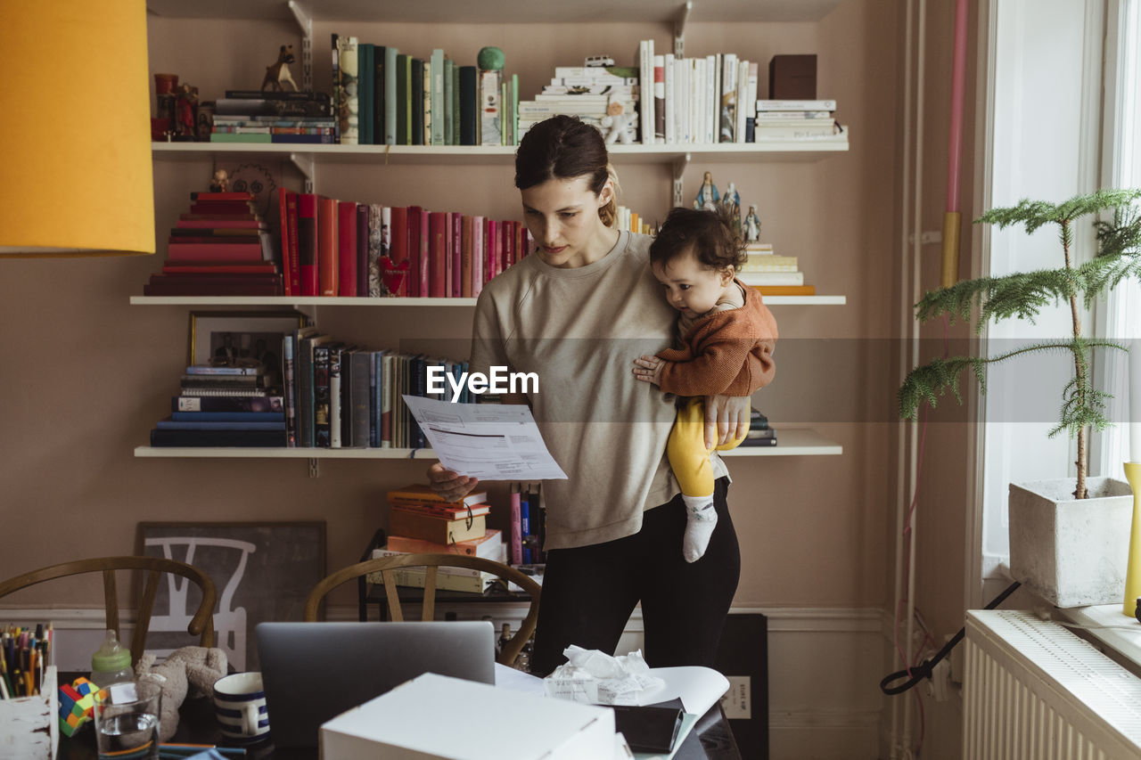 Female professional reading document while carrying son at home office