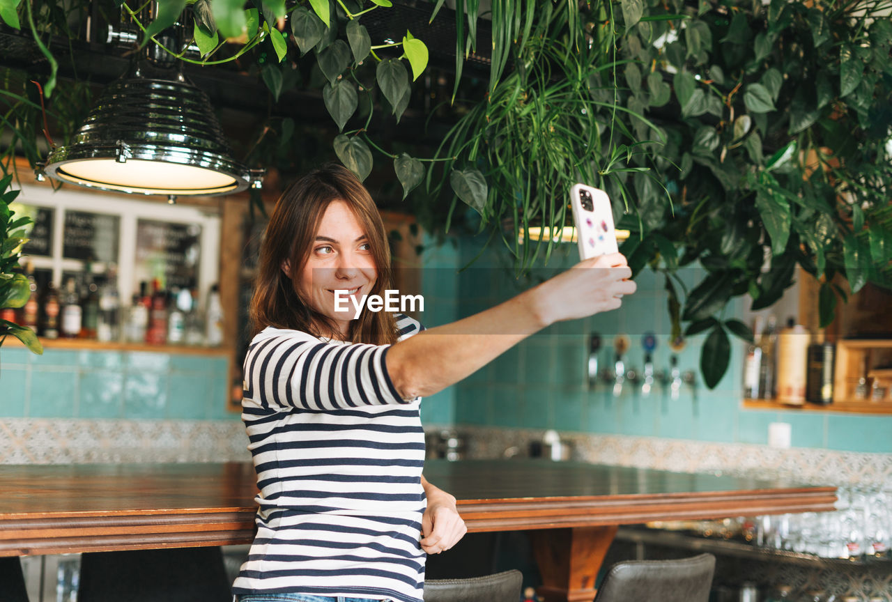 PORTRAIT OF SMILING YOUNG WOMAN USING SMART PHONE