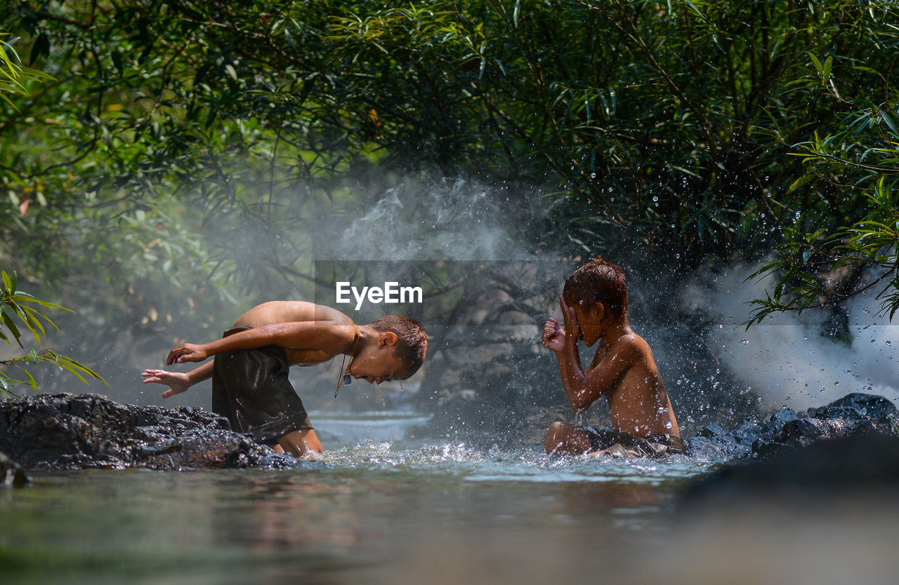 Side view of shirtless brothers bathing in river at forest