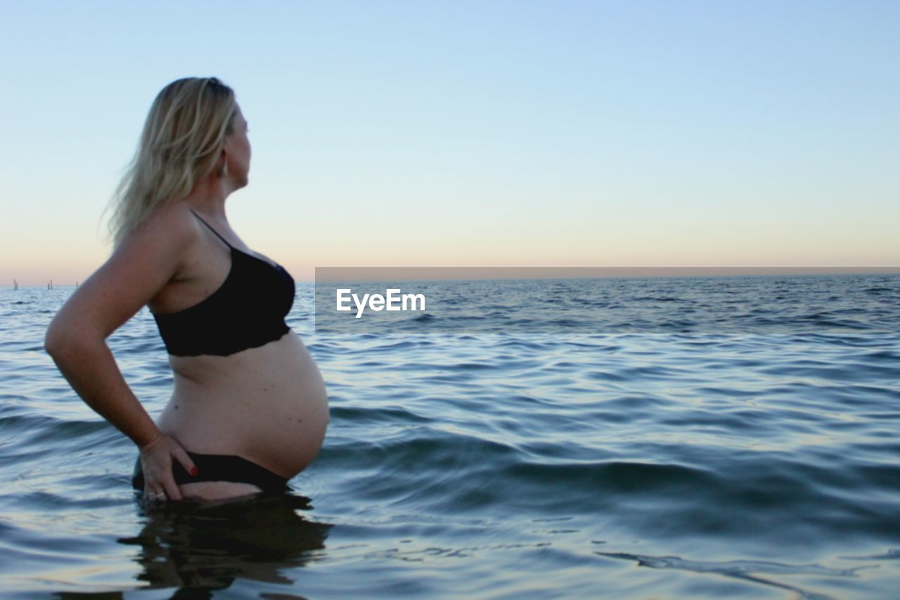 Woman standing at sea shore against clear sky