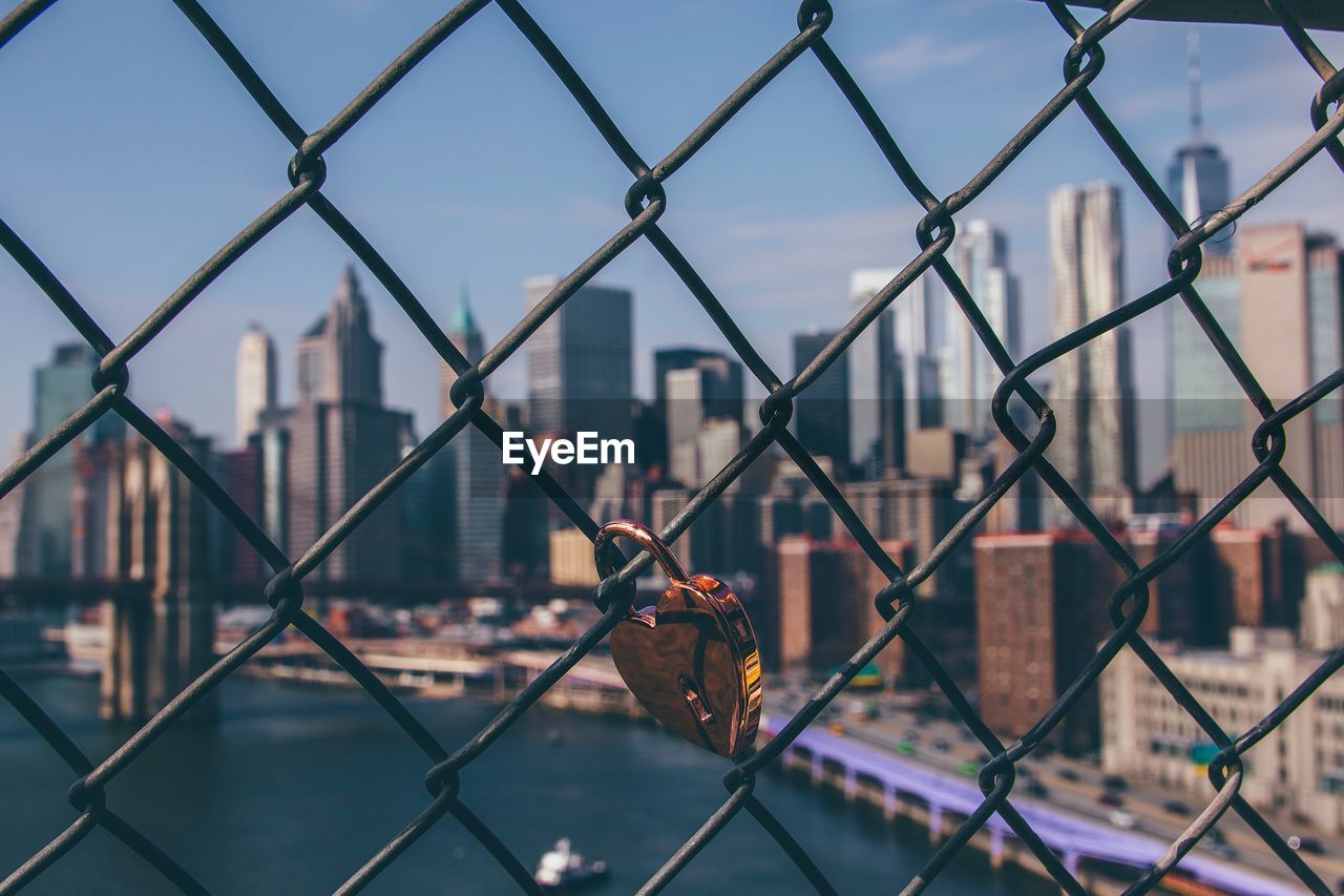 Close-up of padlock attached to chainlink fence against city