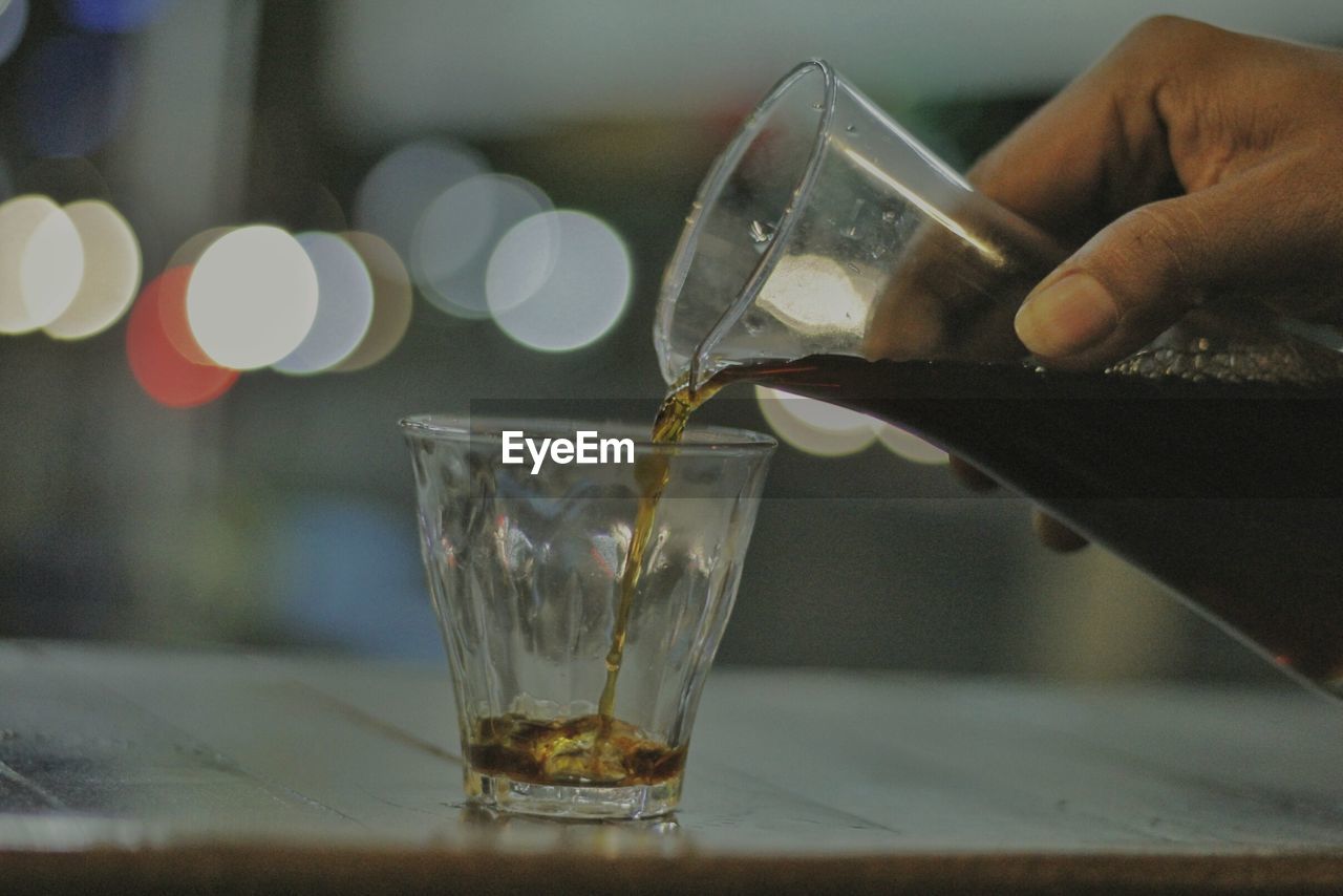 Cropped hand holding pouring drink in glass on table