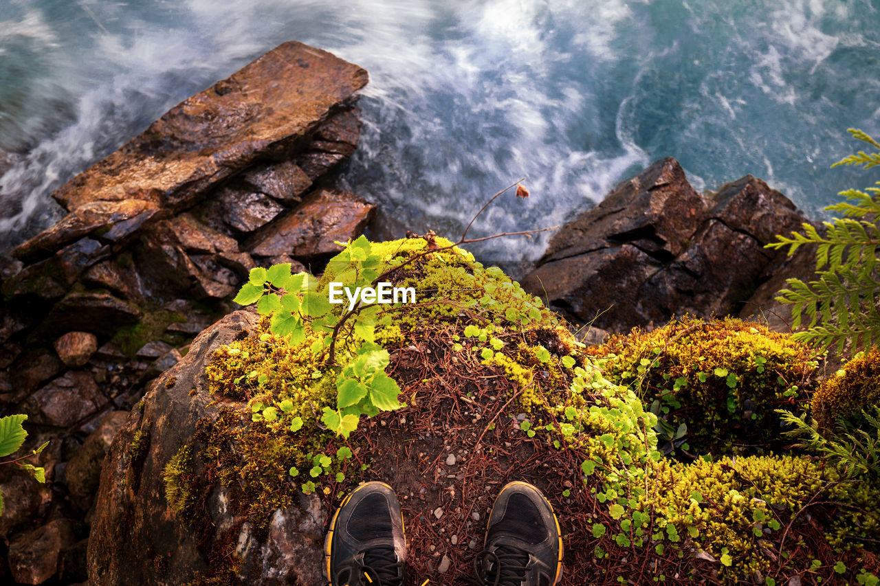 Low section of person standing on cliff by sea