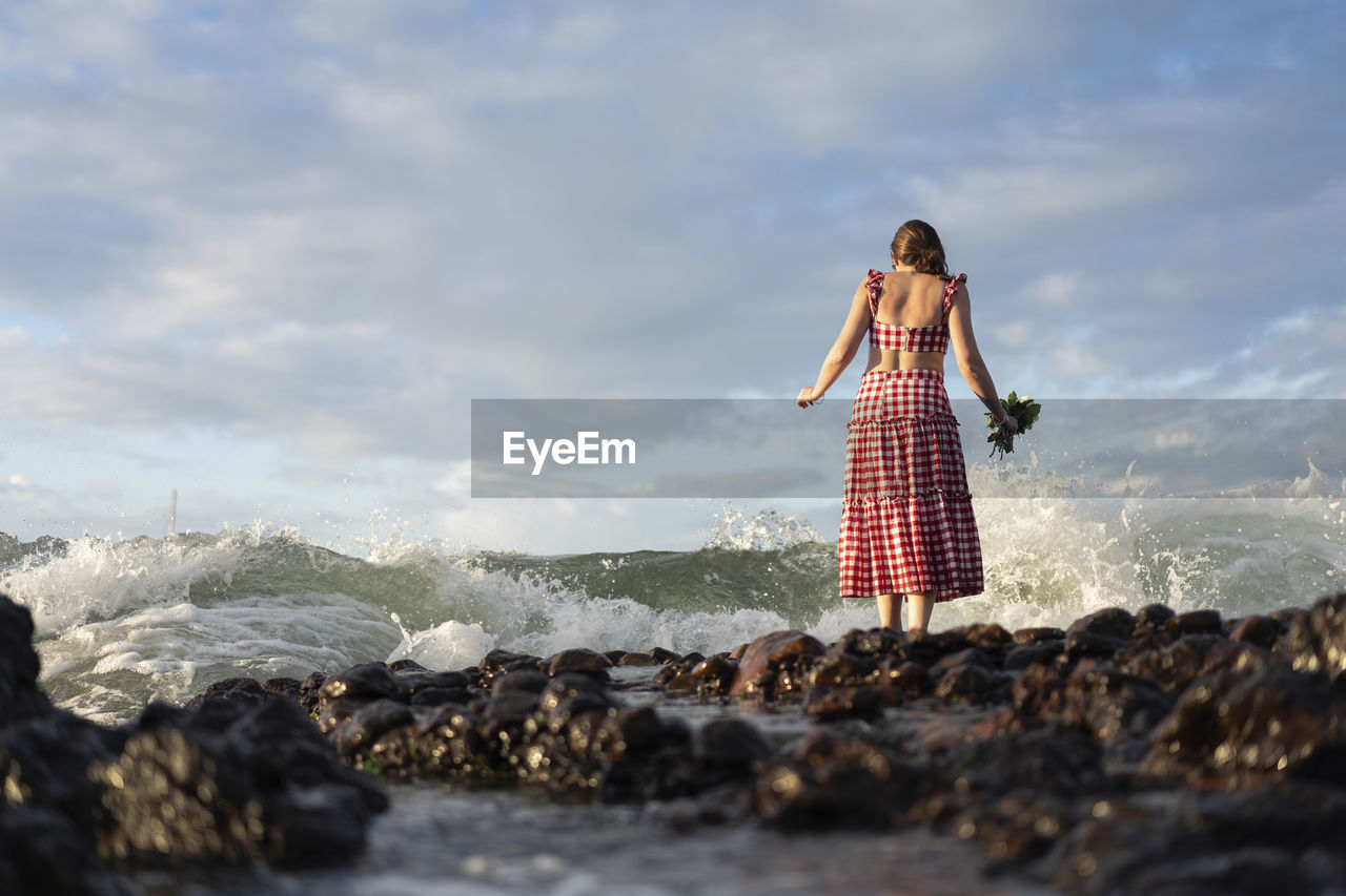 Woman standing on rock by sea against sky