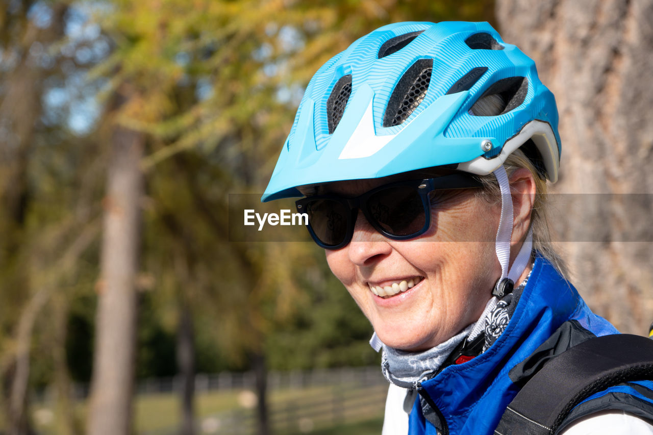 Smiling woman wearing sunglasses and helmet against trees
