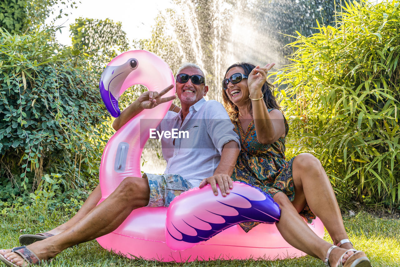 Beautiful smiling middle aged couple having fun sitting on pink flamingo inflatable toy