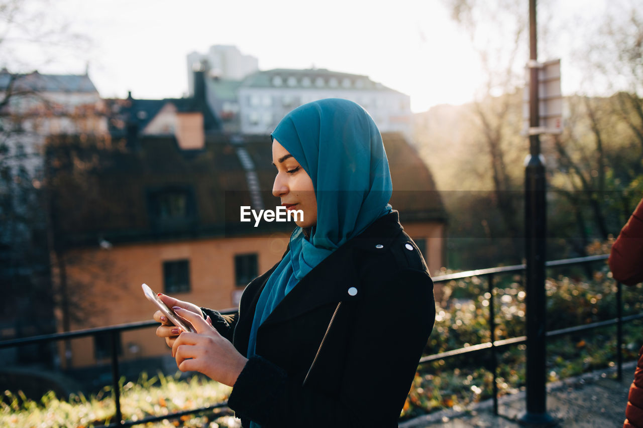 Young muslim woman wearing hijab using smart phone in city