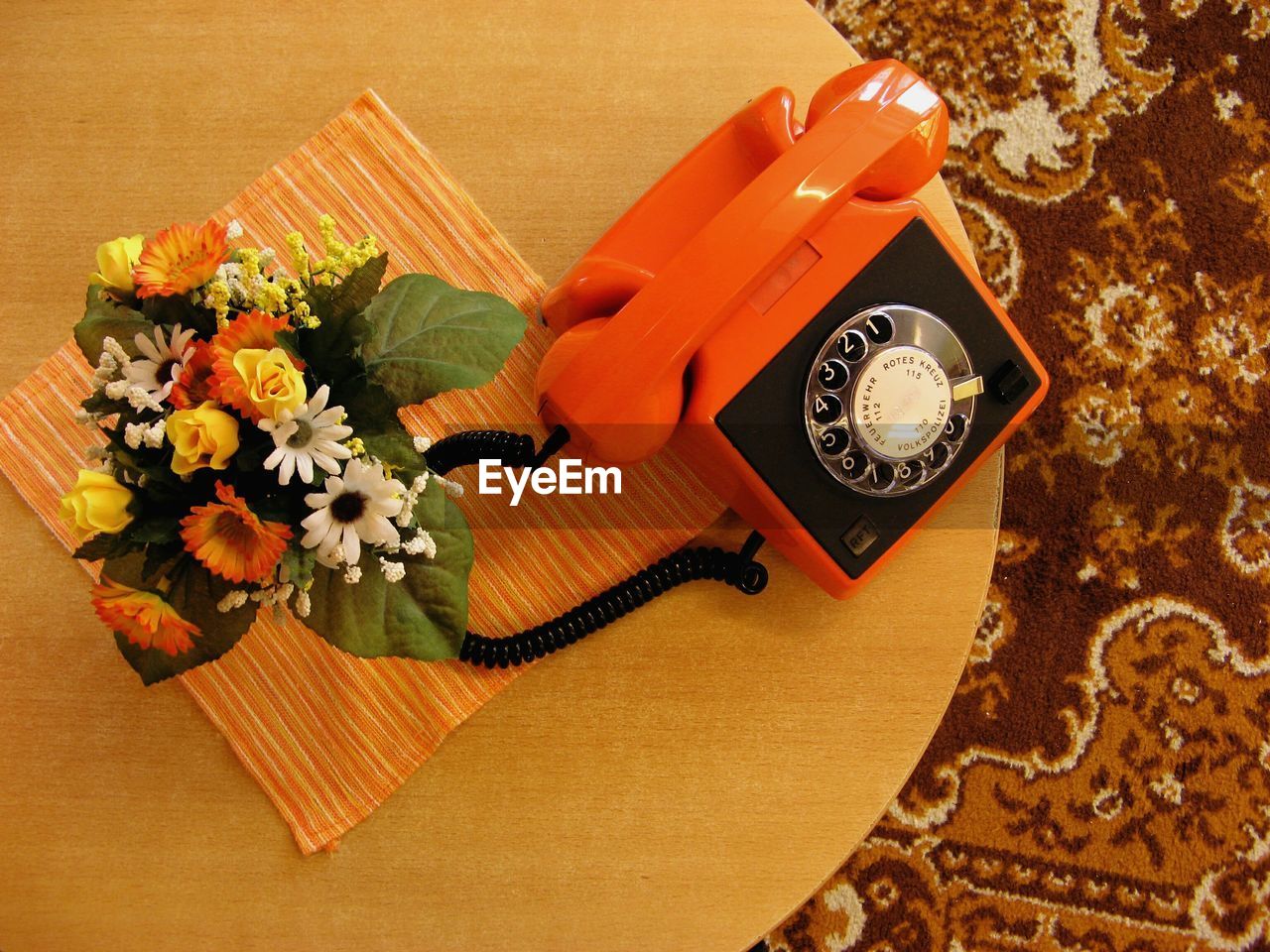 Directly above shot of orange old-fashioned telephone by flowers on table