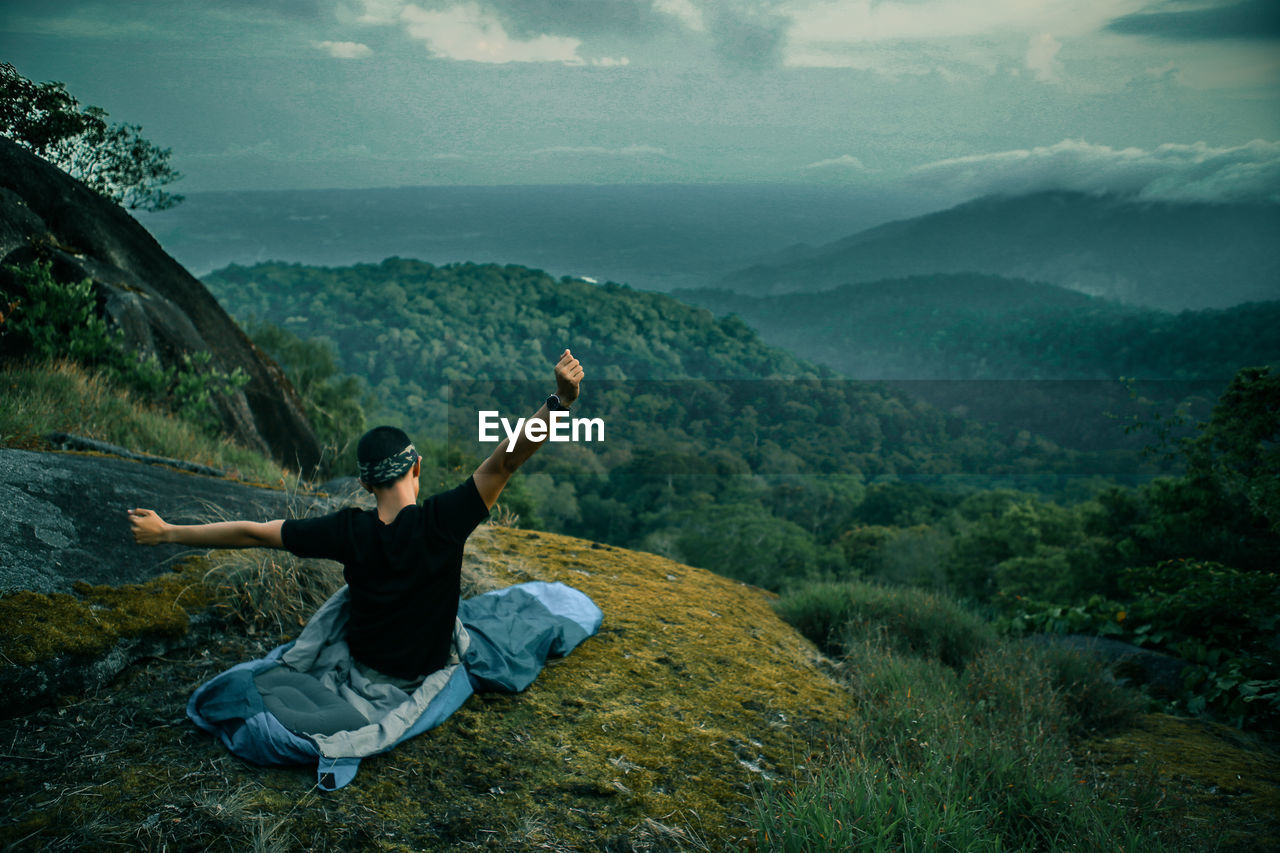 Man stretching hands on mountain against sky