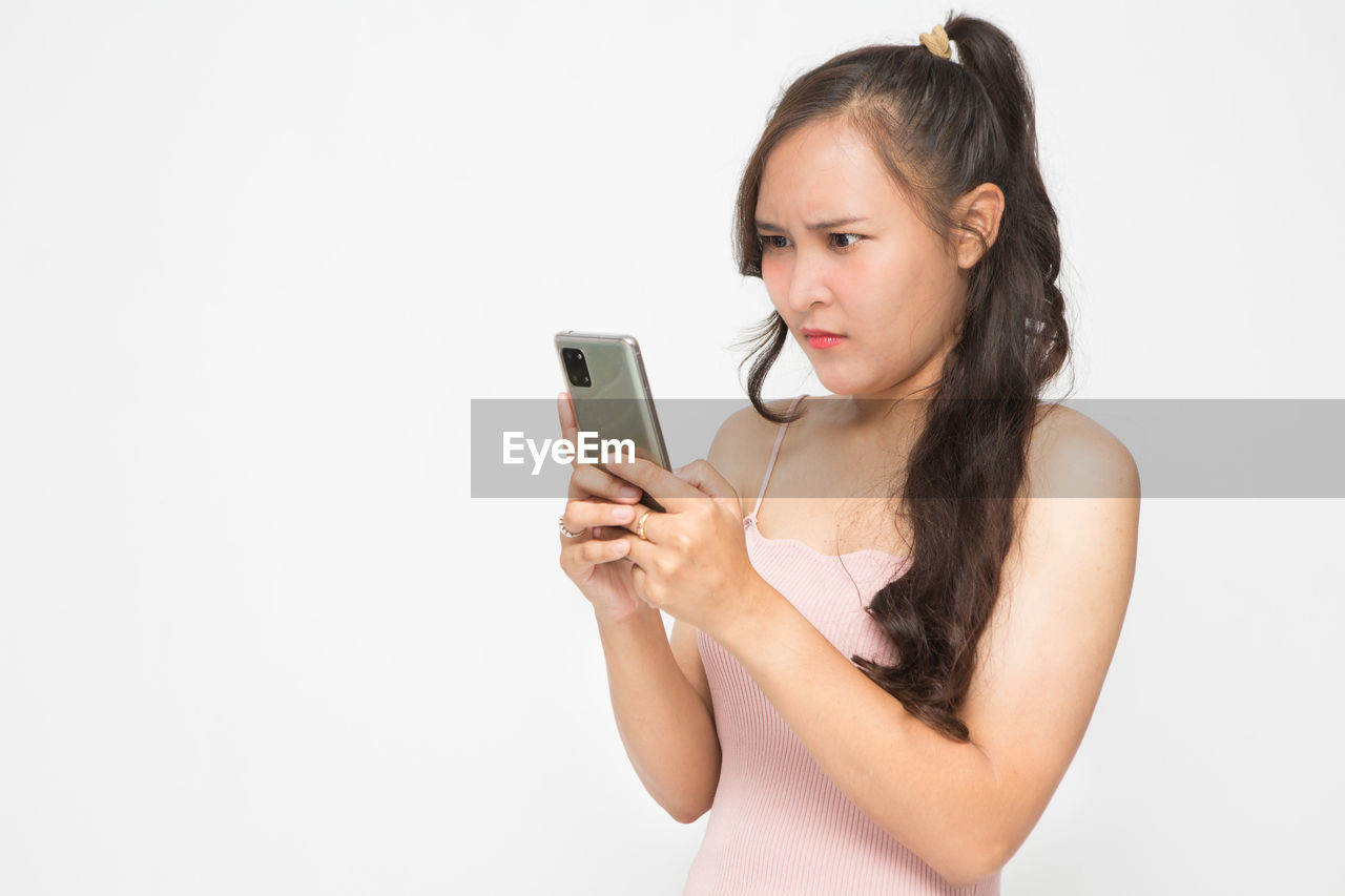 wireless technology, smartphone, portable information device, technology, mobile phone, one person, women, communication, adult, photo shoot, young adult, indoors, studio shot, holding, portrait, telephone, hand, hairstyle, white background, person, finger, selfie, long hair, human face, limb, waist up, lifestyles, activity, arm, using phone, copy space, portability, looking, human hair, brown hair, female, clothing, smiling, fashion, arts culture and entertainment, internet, happiness, human leg, emotion, casual clothing, cut out, mobile app, relaxation, camera