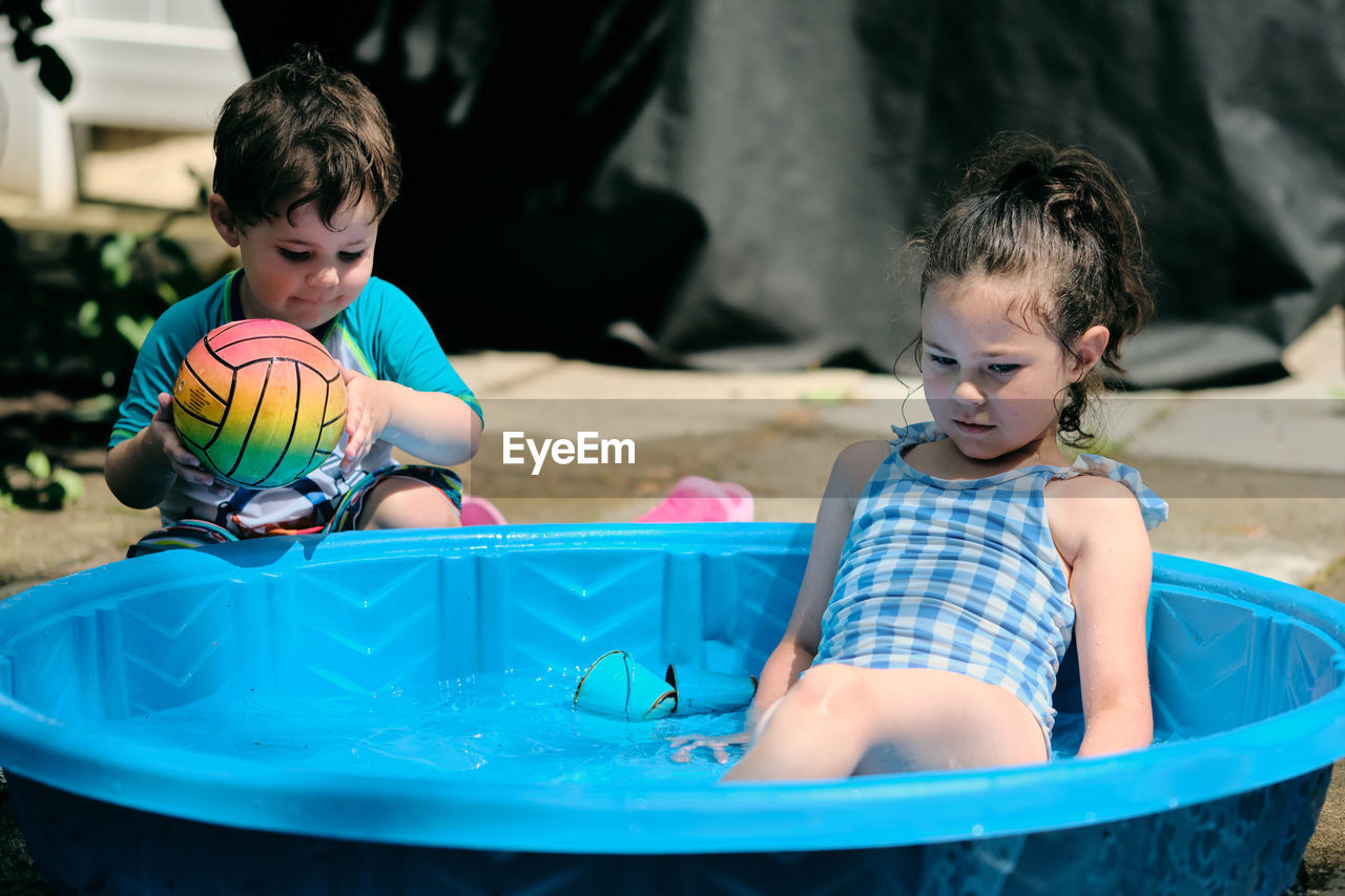 Siblings playing near a water basin in the back yard