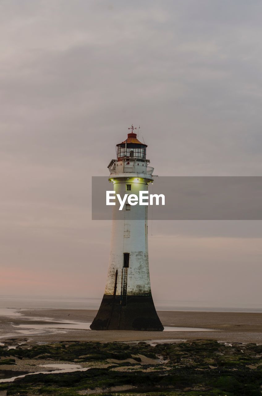 Lighthouse by sea against sky during sunset