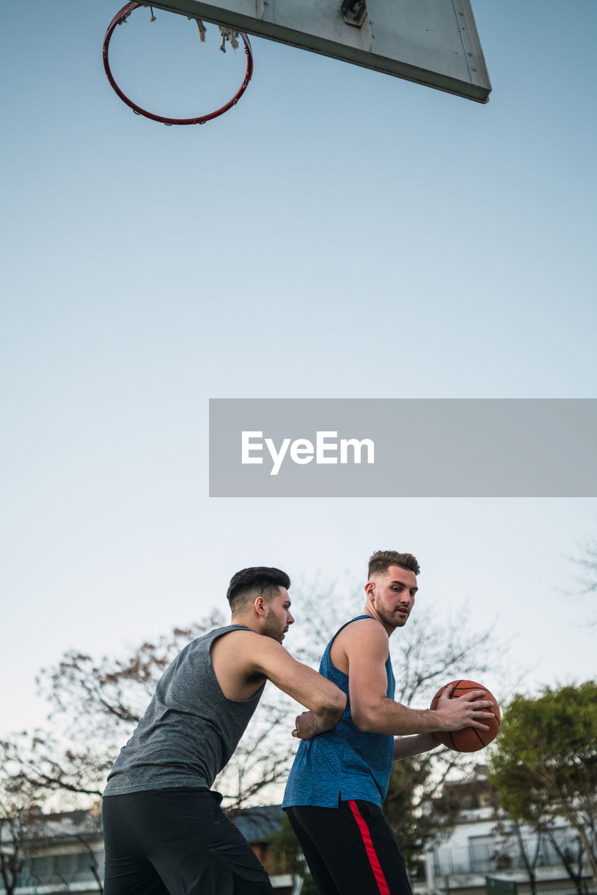 Low angle view of men playing with basketball against clear sky