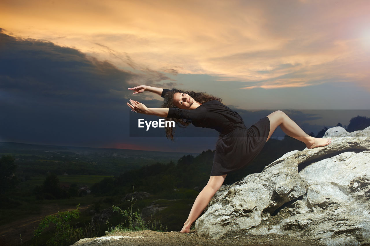 Young woman lying on rock against sky during sunset