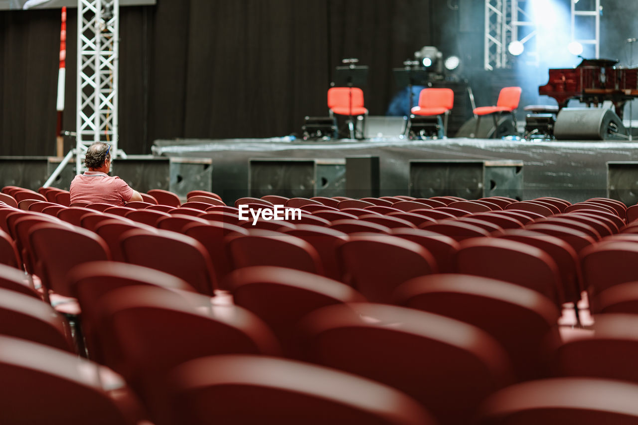 Rear view of man sitting by empty chairs in theater