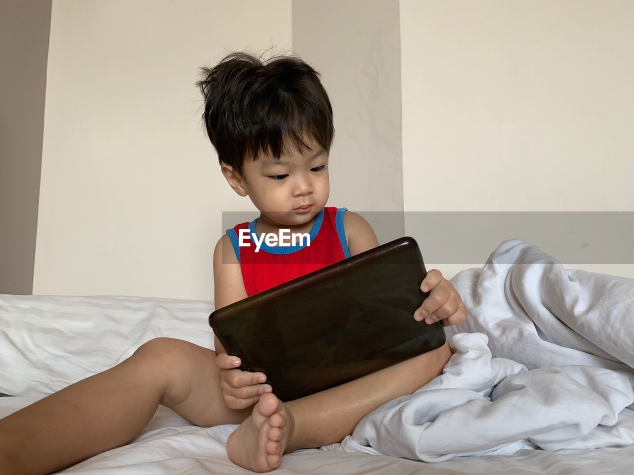 BOY LOOKING AT CAMERA WHILE SITTING ON BED