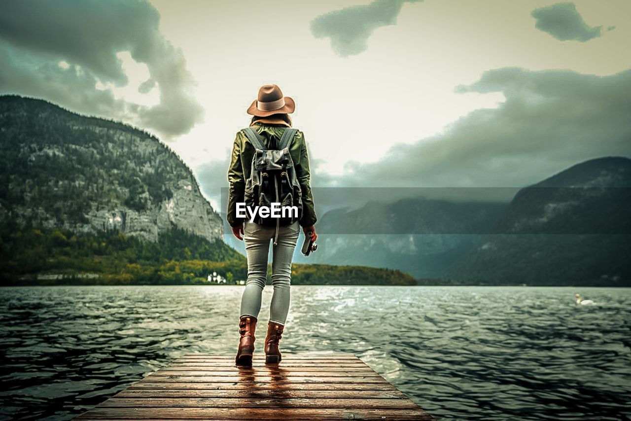 water, one person, sky, mountain, nature, cloud, lake, full length, adult, beauty in nature, reflection, environment, mountain range, scenics - nature, vacation, standing, adventure, trip, leisure activity, clothing, holiday, travel, tranquility, landscape, person, outdoors, footwear, travel destinations, young adult, tranquil scene, land, lifestyles, women, solitude, activity, day, relaxation, forest