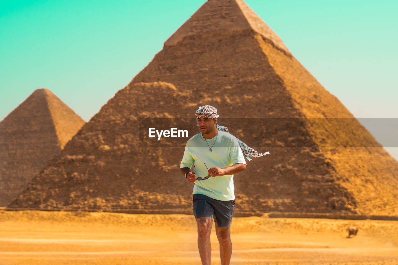 Full length of a man standing on sand at desert with the pyramids behind