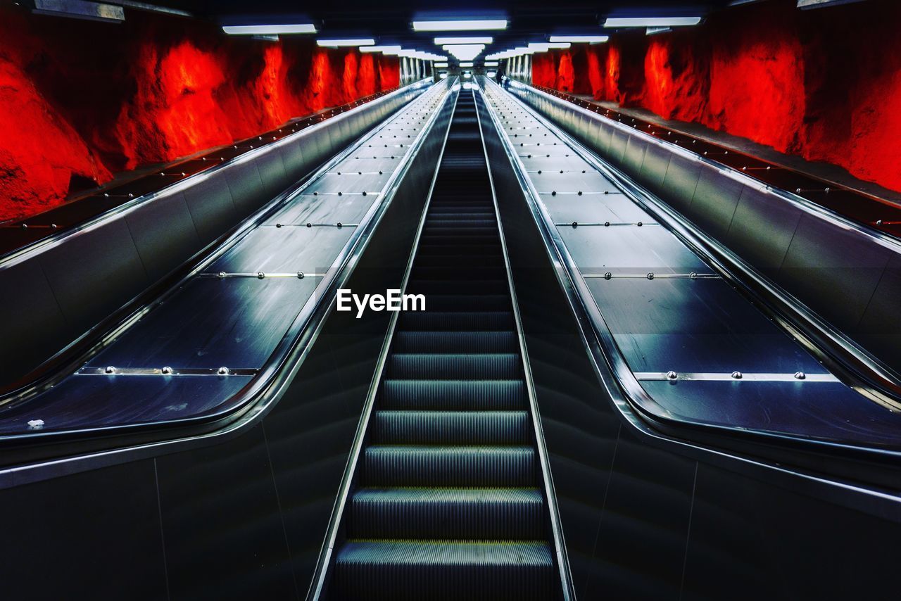 HIGH ANGLE VIEW OF ESCALATOR IN ILLUMINATED UNDERGROUND