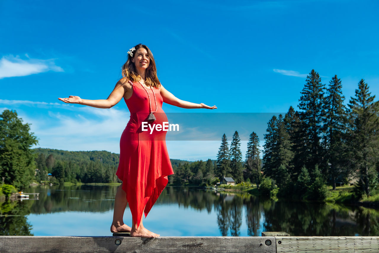 Low angle view of pregnant woman standing against lake