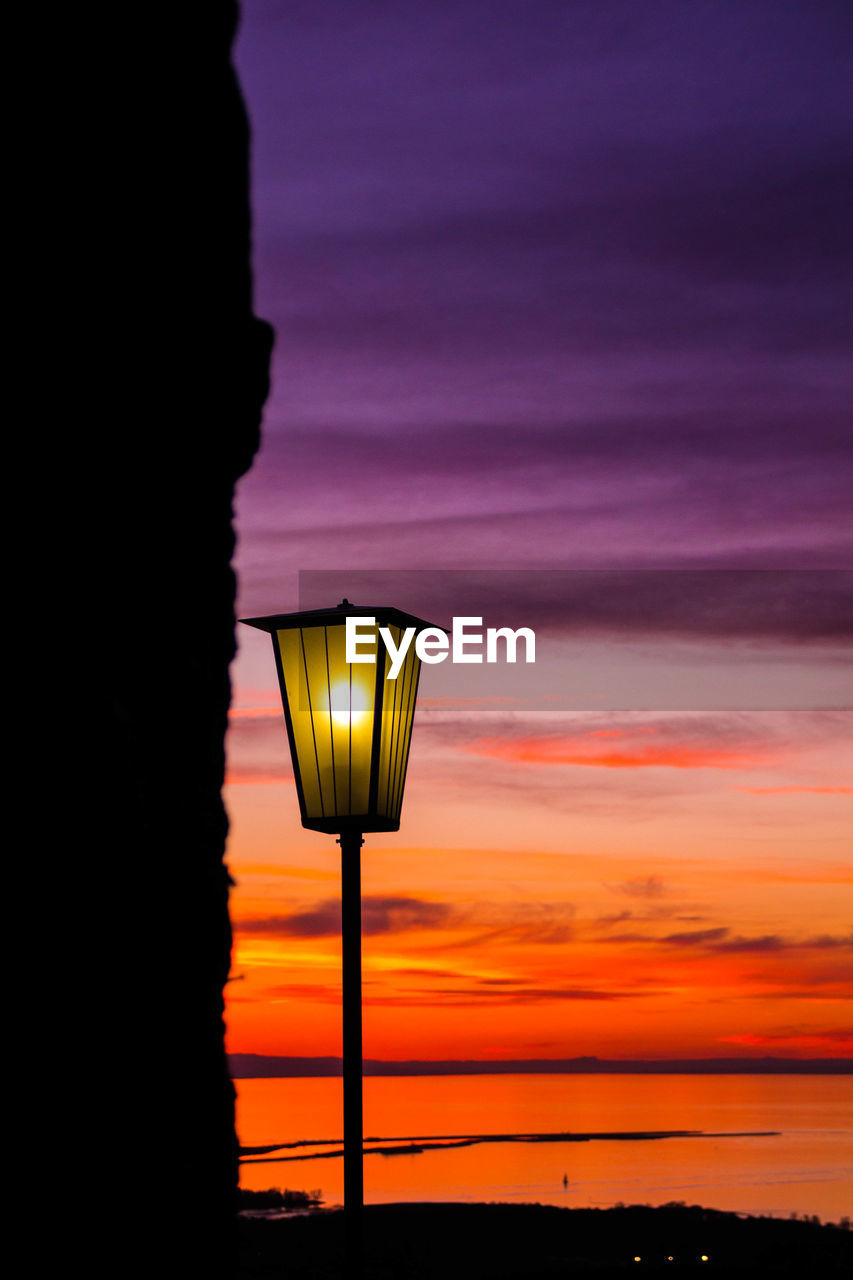 Illuminated gas light against dramatic sky during sunset