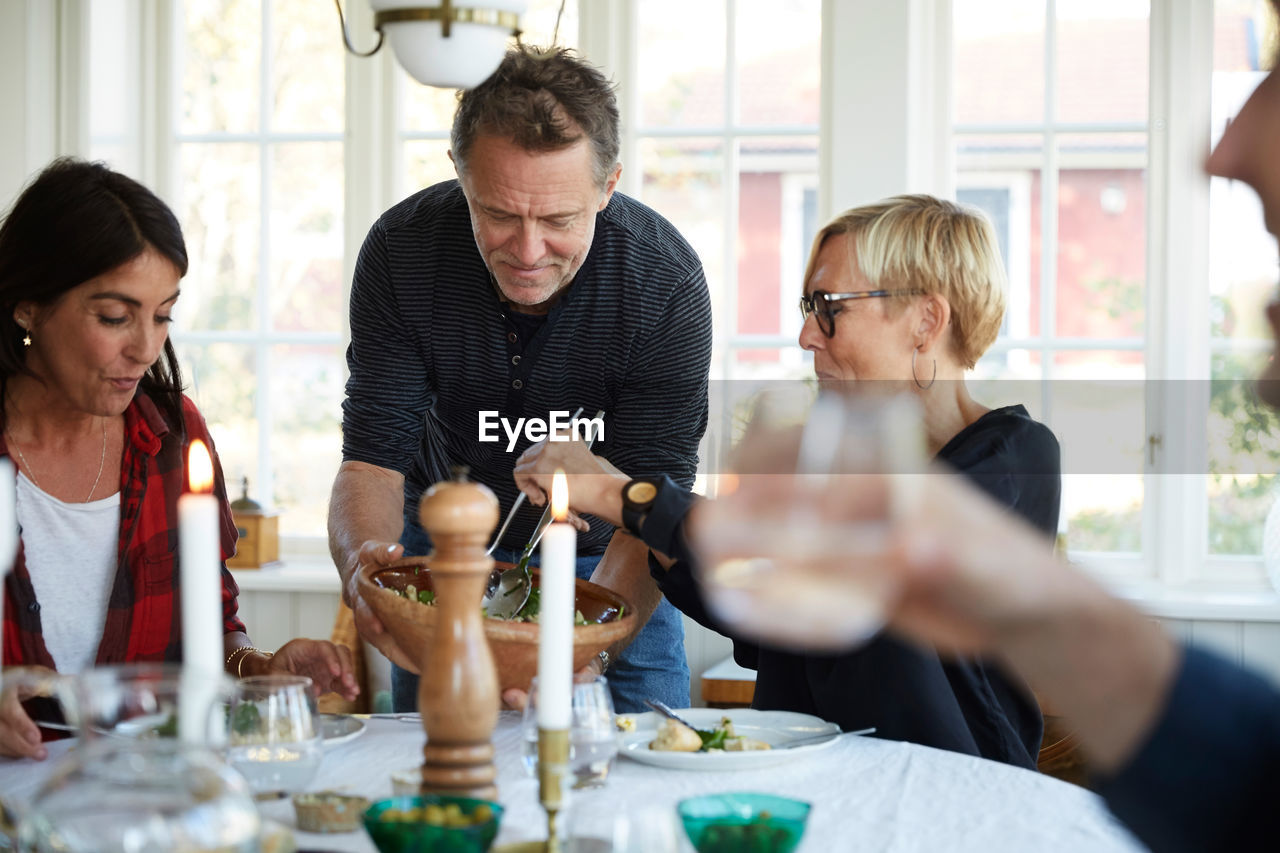 Mature man serving food to female friends at home