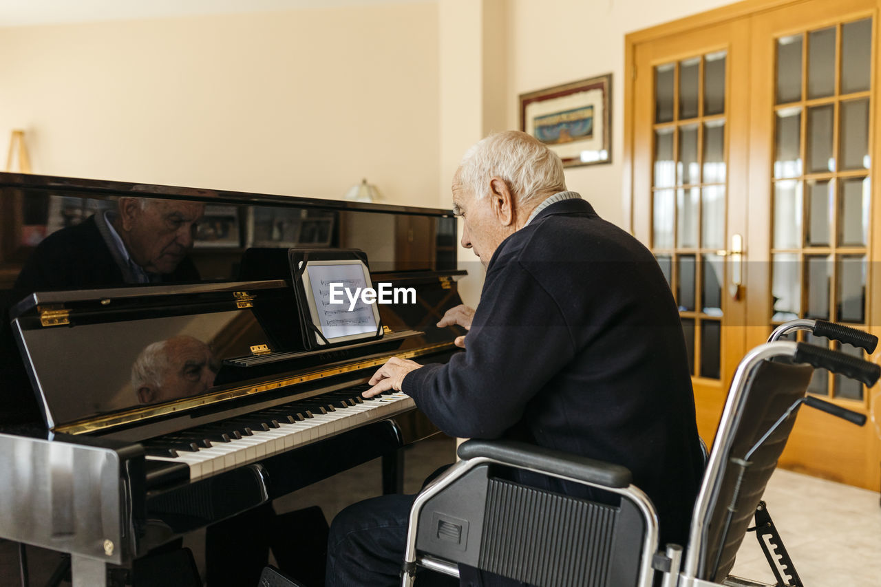 Senior man sitting in wheelchair playing piano at home