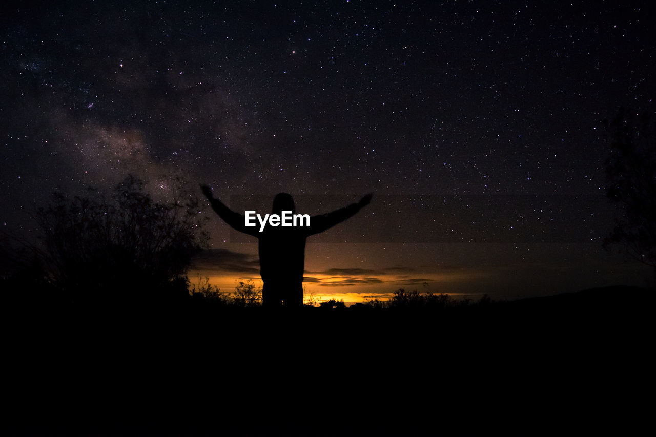 SILHOUETTE OF MAN STANDING ON FIELD AGAINST SKY AT NIGHT