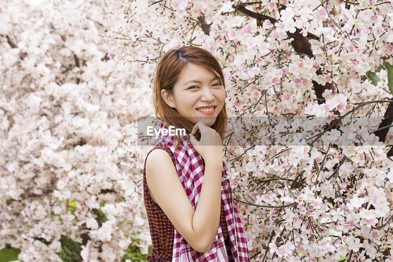 Portrait of smiling woman standing against pink cherry blossoms