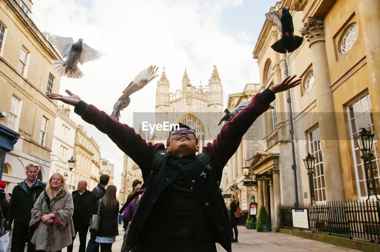 Man raising arms while birds flying against church